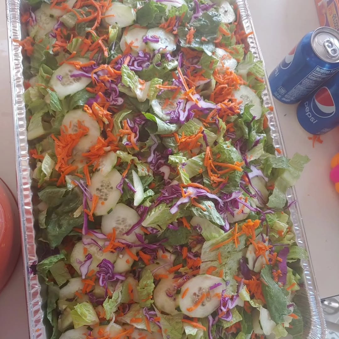 A large foil tray of green salad with cucumber, carrot and red cabbage